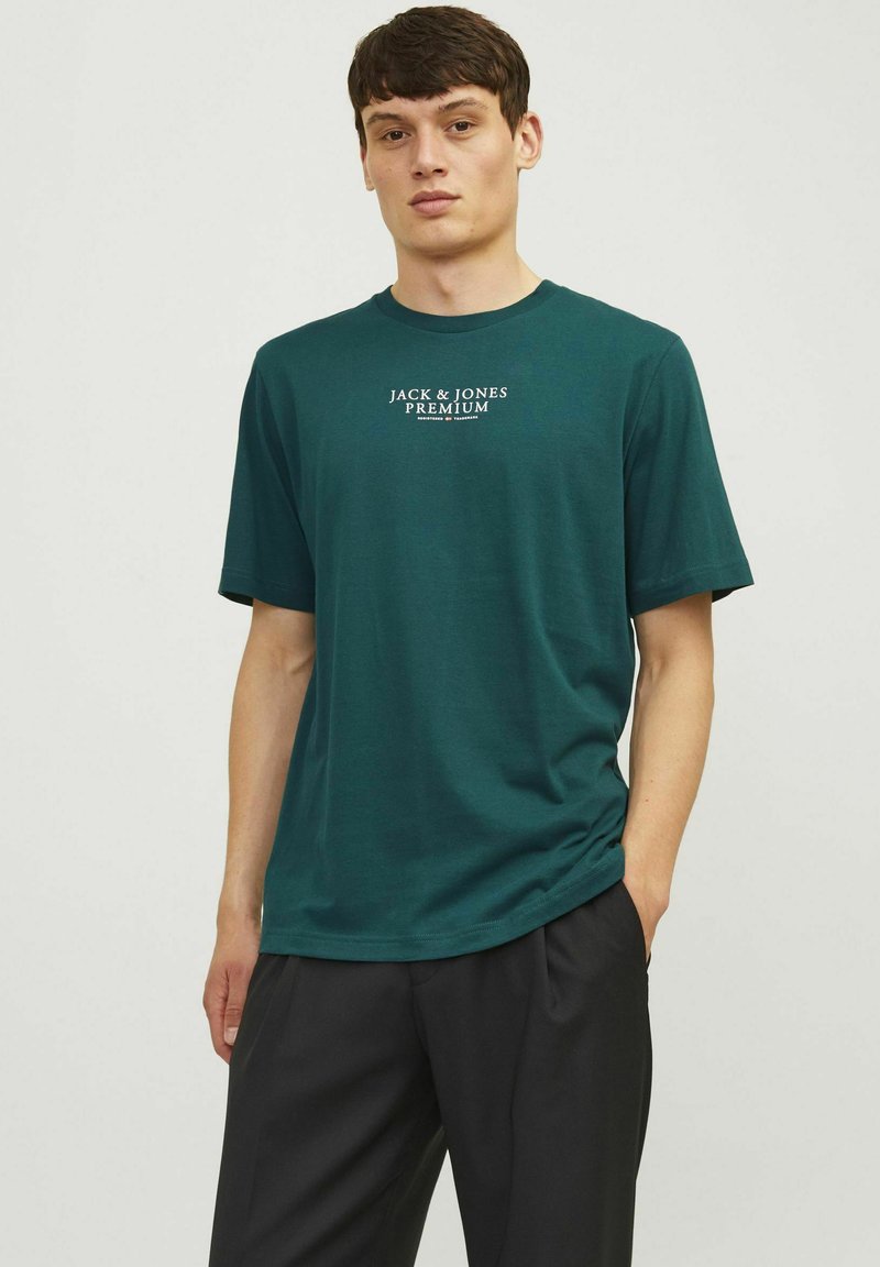 Vihreä puuvillapaita, jossa on pyöreä kaula-aukko, lyhyet hihat ja valkoinen "JACK & JONES PREMIUM" -grafiikka rinnassa. Pehmeä tekstuuri.