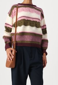 Flerfärgad stickad tröja med horisontella ränder i rosa, grönt, krämfärgat och vinröd med olika texturer; kombinerad med mörka byxor och en brun väska.