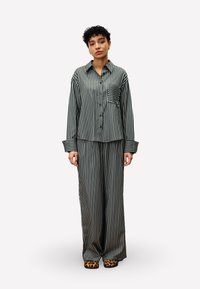 Green and white striped pajama set with a button-up shirt featuring a chest pocket and wide-legged pants, paired with leopard print footwear.