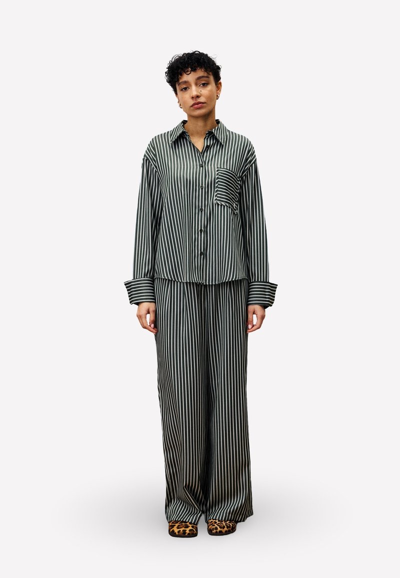Green and white striped pajama set with a button-up shirt featuring a chest pocket and wide-legged pants, paired with leopard print footwear.