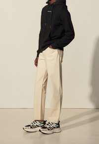 Felpa nera con cappuccio e tasca frontale, pantaloni larghi color crema e sneakers chunky multicolori con motivi geometrici e texture.