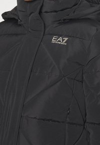 Czarna kurtka puchowa z pikowanym wzorem, posiadająca wysoki kołnierz, kieszenie na zamek oraz tłoczone logo EA7 na piersi.