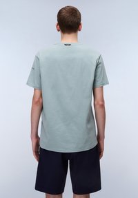 T-shirt in cotone verde chiaro con collo rotondo, maniche corte e orlo dritto, abbinata a pantaloni corti scuri. Nessun motivo o grafica visibili.