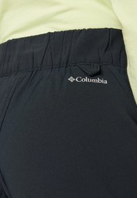 Zwarte sportbroek met een elastische tailleband, voorzien van een trekkoord en een wit Columbia-logo aan de zijkant. Glad, rekbaar materiaal.