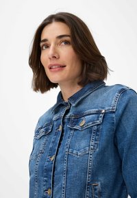 Giacca di jeans di un azzurro chiaro con chiusura a bottoni, due tasche sul petto, colletto classico e dettagli di cucitura visibili in tutta la giacca.