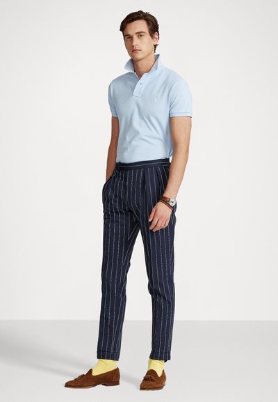 Light blue polo shirt with short sleeves, navy pinstriped trousers, yellow socks, and brown suede loafers, featuring a collar and polished watch.