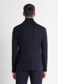Blazer su misura blu scuro con colletto strutturato, spacco singolo sul retro e polsini con bottone. Tessuto in lana liscia.