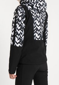 Czarna kurtka z wzorzystym, białym i czarnym kapturem oraz rękawami z geometrycznymi wzorami; gładka tekstura i dopasowany krój.