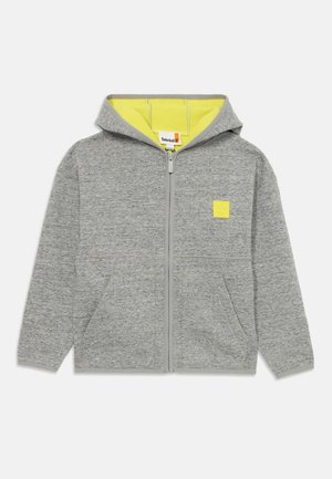 Hoodie zippé gris avec une doublure jaune. Présente un petit patch logo sur la poitrine et deux poches avant. Texture lisse.