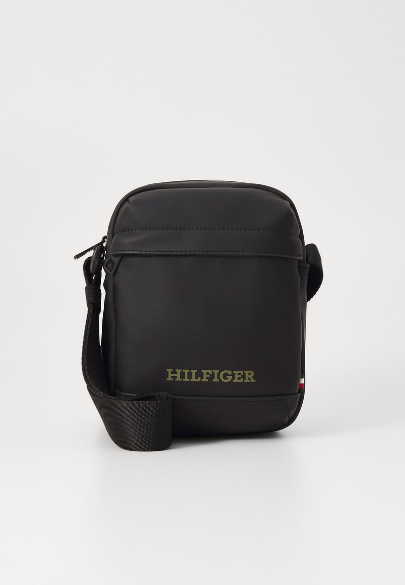 Borsa crossbody nera in materiale sintetico con chiusura a zip, caratterizzata da un prominente logo "HILFIGER" in oro e una tracolla texturizzata.
