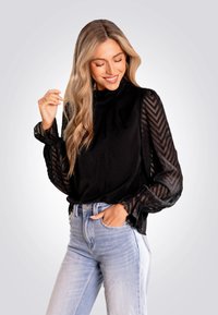 Top noir avec des manches transparentes et à motifs, et un col montant, associé à un jean taille haute bleu clair. Tissu lisse avec un design texturé.