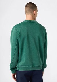 Sudadera verde con cuello redondo, mangas largas y puños de canalé, con una textura suave y un aspecto ligeramente desvanecido.