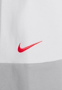 Gros plan sur un tissu blanc et gris avec un petit logo Nike Swoosh rouge brodé sur la partie blanche.