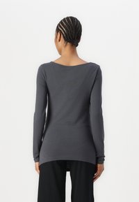 Camisa de manga larga, gris, con cuello redondo, hecha de una tela suave, con un dobladillo trasero más largo y un diseño ajustado.