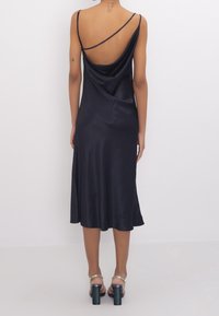 Navy slip dress in lightweight satin with a draped back and thin shoulder straps, featuring a flowing hem and minimalistic design.