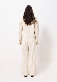 Cremfarbener, taillierter Anzug mit vertikalen Nadelstreifen, strukturierten Schultern und weit geschnittenen Hosen mit umgeschlagenen Säumen. Rückansicht gezeigt.