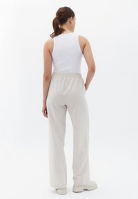 Volné světle béžové kalhoty s elastickým pasem, v kombinaci s bílým topem bez rukávů. Hladká tkanina a rovný střih nohavic.