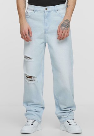 Lichtblauwe spijkerbroek met gescheurde knieën, recht gesneden en een iets losse fit. Gepaard met witte sneakers.