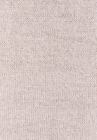 Gros plan d’un tissu tricoté doux beige clair montrant des mailles verticales et horizontales avec une texture subtile et de légères variations de couleur.