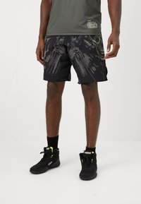 Shorts de sport noirs avec un motif graphique gris, associés à des chaussures de sport noires avec des accents vert néon et des chaussettes de cheville noires.