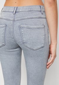 Vaqueros de mezclilla azul claro con una textura suave, que cuentan con dos bolsillos traseros y un diseño ajustado que se adapta al cuerpo.