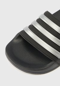 Zwarte slippers met drie horizontale zilveren strepen, een gestructureerde zool en een glad bovenoppervlak. Ontworpen voor comfort en dagelijks gebruik.