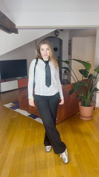 Juodos kelnės derinamos su baltu ir juodu dryžuotu ilgomis rankovėmis marškinėliu, suveržta juoda kaklaraište, sidabriniais batais ir juoda peties rankine.