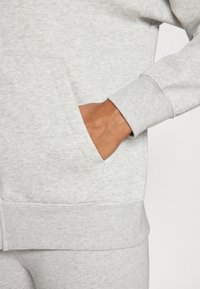 Ljusgrå sweatshirt med ett framfick och ribbade ärmmuddar. Mjuk textur och avslappnad design som visar en figursydd silhuett.