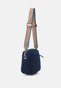 Petit sac bandoulière en tissu bleu marine avec une sangle rayée multicolore réglable et des détails argentés sur la fermeture éclair et le clip.