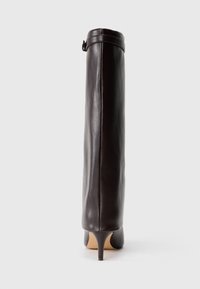 Botas de cuero marrón de tacón, hasta la rodilla, con un diseño ajustado, puntera redonda y un tacón de aguja estrecho. Detalle de correa ajustable en la parte superior.