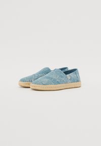 Scarpe slip-on azzurro chiaro in tessuto texturizzato con un motivo a foglie, dettagli in corda di juta attorno alla suola e design con tallone chiuso.
