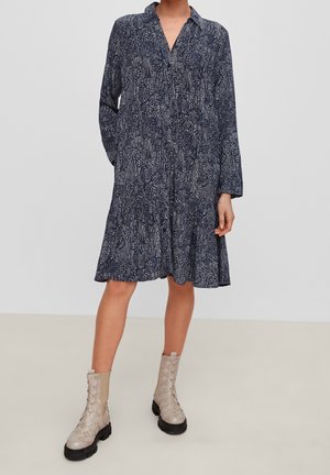 Langärmliges, marineblaues Kleid mit kragenförmigem Ausschnitt und gemusterter Textur. Verfügt über einen ausgestellten Saum, Seitenentaschen und wird mit beigen Knöchelstiefeln kombiniert.