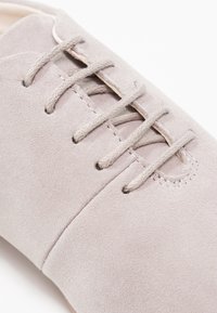 Gros plan sur une chaussure en daim beige clair avec un détail lacé assorti sur une surface lisse.