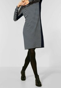 Randig klänning med marinblå och vita horisontella ränder, långa ärmar och en avslappnad passform. Bärs med svarta opaka strumpbyxor och ankelstövlar.