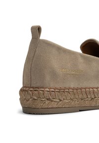 Beige suede slip-on shoe with a woven jute sole, featuring a rounded toe and subtle gold branding on the side.