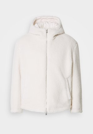 Bílá kabát z umělé kožešiny s kapucí, plným předním zipem a bočními kapsami. Má měkký, texturovaný povrch a rovný střih.