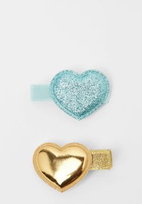 Dvě sponky do vlasů: jedna je světle modrá třpytivá ve tvaru srdce s stuhou; druhá je zlatá kovová srdce se zlatým texturovaným páskem.