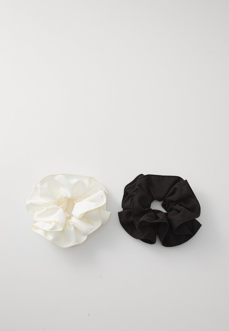 Două elastice din satin, unul alb și unul negru, cu un design volan și textură netedă, expuse pe un fundal alb simplu.