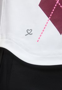 Λευκό ύφασμα με μικρό γκρι αφηρημένο σχέδιο καρδιάς κοντά στο στρίφωμα, δίπλα σε βυσσινί και ροζ γεωμετρικό διακοσμητικό μοτίβο με τελείες.