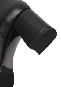 Chaussure à talons hauts en cuir noir avec un bout rond et un talon carré. Présente une texture lisse et une base de talon mate contrastante.