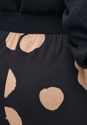 Nahaufnahme eines schwarzen Stoffes mit beigen, herzförmigen Mustern und einem gerippten schwarzen Bund.