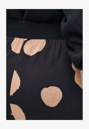 Close-up van zwarte stof met beige hartvormige patronen en een geribbelde zwarte tailleband.