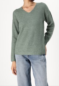 Ljusgrön ribbad stickad tröja med V-ringning och långa ärmar, i kombination med ljusa denimbyxor. Mjuk textur, avslappnad passform.