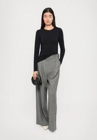 Black long-sleeve top, gray wide-leg trousers with pleats, and a small black bag. White pointed-toe shoes. Plain background.