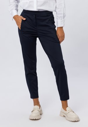 Pantalons slim-fit bleu marine en tissu léger, dotés de poches latérales et d'une texture lisse, associés à des chaussures beiges à enfiler.