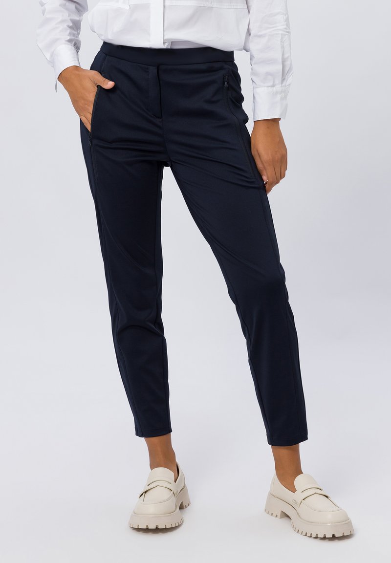 Marineblauwe slim-fit broek gemaakt van lichte stof, met zijzakken en een gladde textuur, gecombineerd met beige instapschoenen.