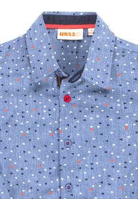 Camicia blu per bambini con piccoli motivi a triangolo rossi, bianchi e blu navy e bottoni blu e rossi, etichettata taglia 4 anni.