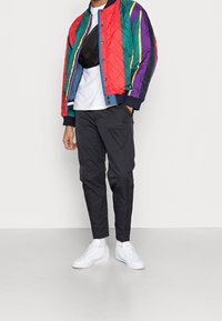 Colorful quilted bomber jacket with green, red, purple, and yellow stripes, paired with black slim-fit pants and white sneakers.
