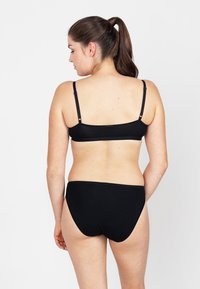 Zwarte bralette met dunne verstelbare bandjes, gecombineerd met bijpassende zwarte bikini-slipjes. Eenvoudig ontwerp met naadloze randen en een zachte textuur.