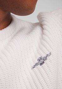 Maglione bianco a maglia con un motivo testurizzato e un piccolo ricamo di un'aquila nera sul petto sinistro. Collo rotondo, vestibilità comoda.
